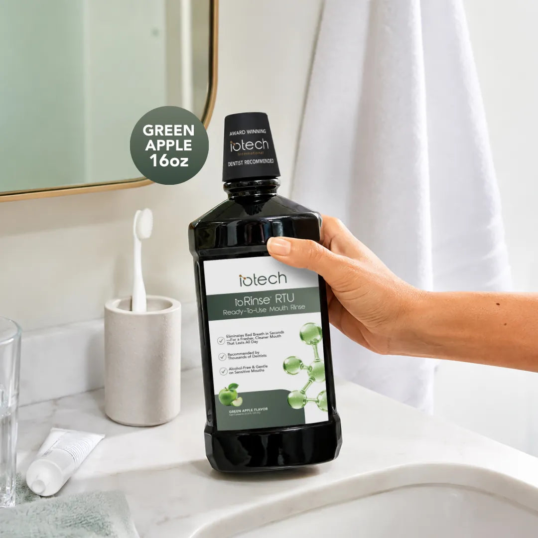 Hand holding ioRinse RTU Green Apple 16 oz bottle at a bathroom sink