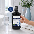 Hand holding ioRinse Ultra Soft Mint 16 oz bottle at a bathroom sink
