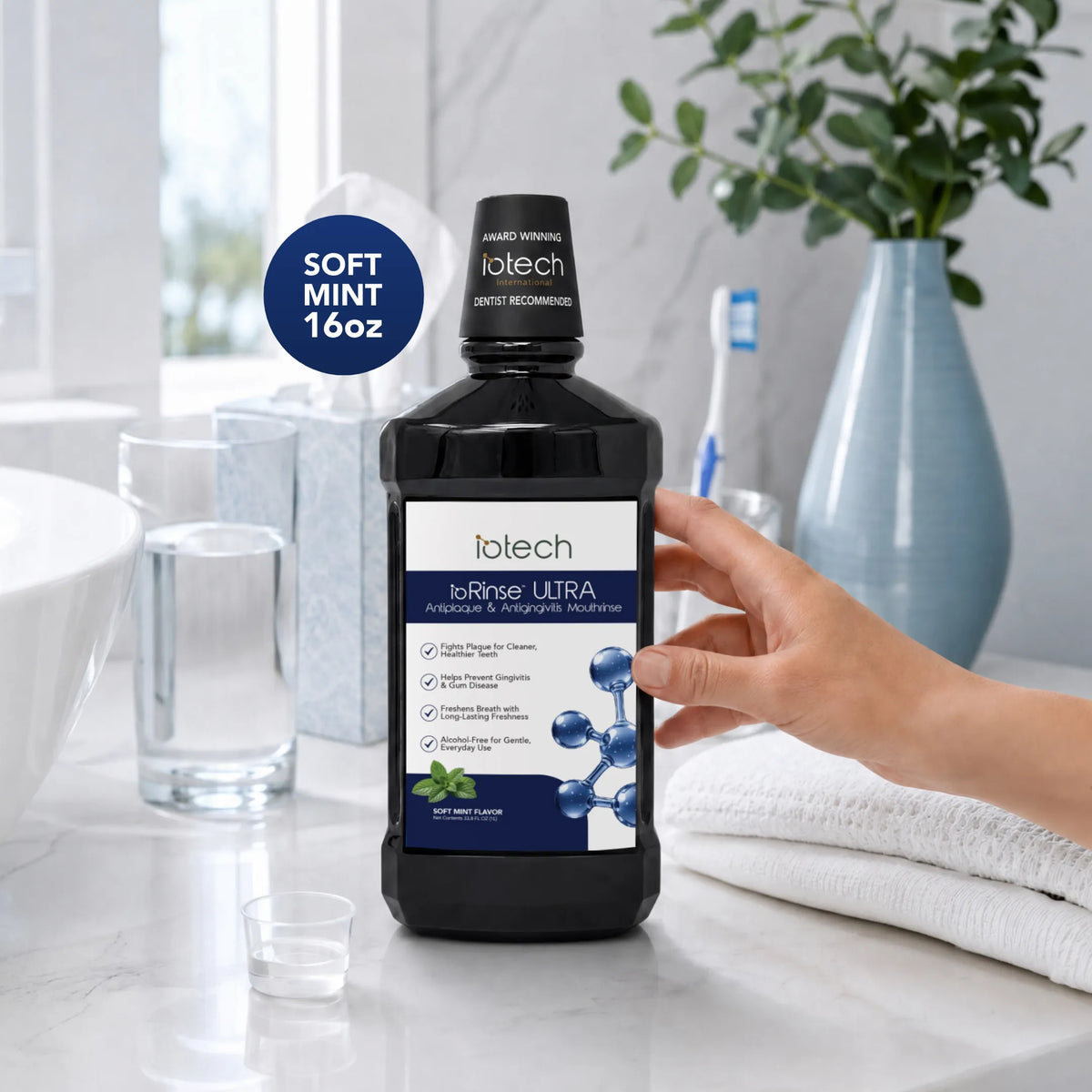 Hand holding ioRinse Ultra Soft Mint 16 oz bottle at a bathroom sink
